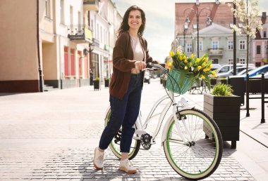 Beautiful woman with bicycle and bouquet of yellow tulips on city street