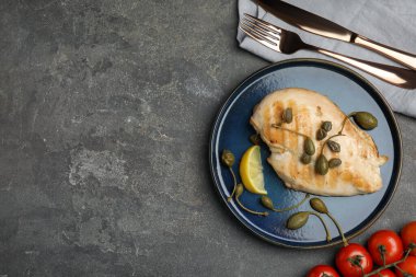 Gri masada servis edilen kapari ve limon dilimli nefis pişirilmiş tavuk filetosu. Metin için boşluk