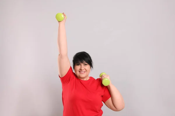 幸せな太りすぎ成熟した女性あります演習とともにダンベル上の灰色の背景 — ストック写真