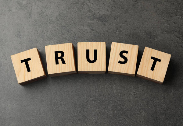 Word TRUST made with wooden cubes on grey table, flat lay