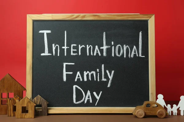 带有文字的小黑板国际家庭日 木制房屋模型 人物和玩具汽车在褐色桌子上的红色背景 — 图库照片