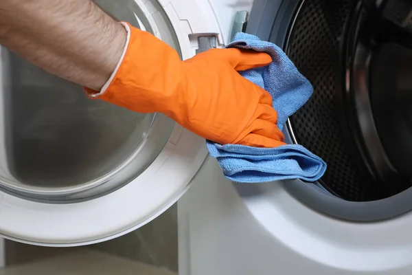 Man cleaning empty washing machine with rag, closeup