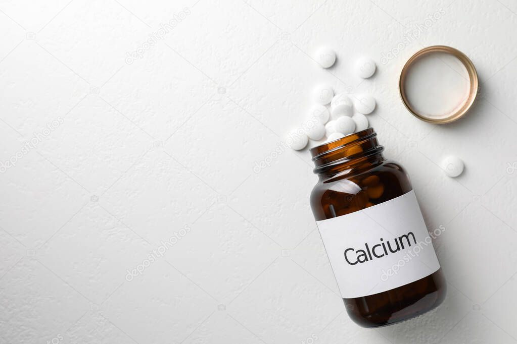 Overturned bottle of calcium supplement pills on white table, flat lay. Space for text