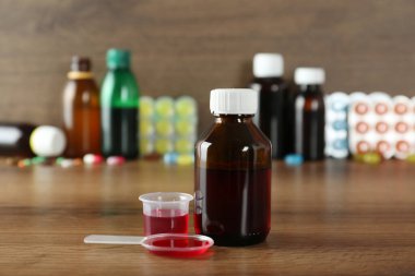 Şişe, kaşık ve tahta masada öksürük şurubuyla ölçme kabı.