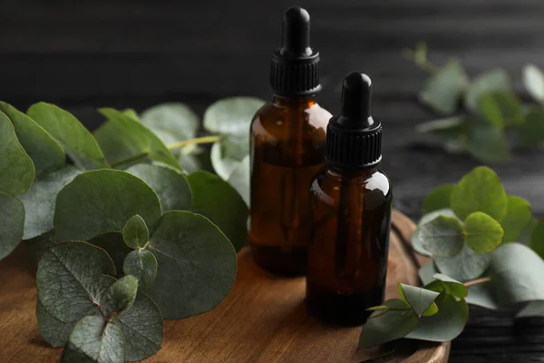Flaschen Mit Ätherischem Eukalyptusöl Und Pflanzenzweige Auf Holzteller — Stockfoto