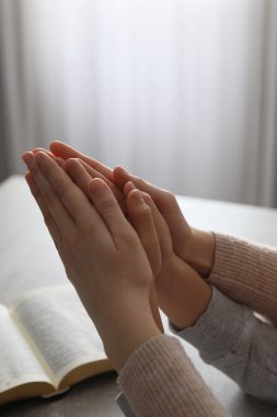 Oğlan ve vaftiz ebeveyni kapalı alandaki gri masada birlikte dua ediyor.