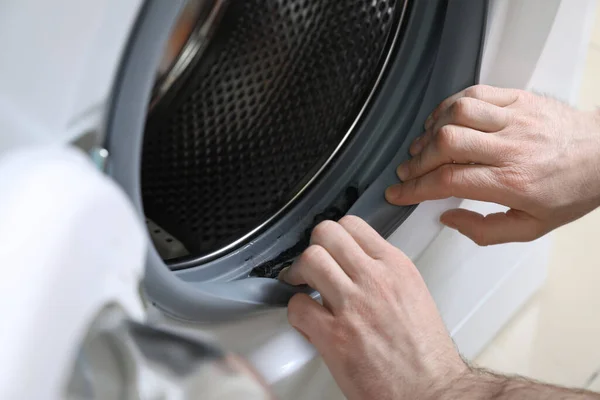 Man cleaning dirty seals of washing machine, closeup