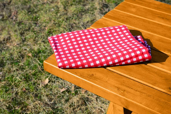 公园里木制野餐桌上折叠的红白相间的格子桌布 — 图库照片