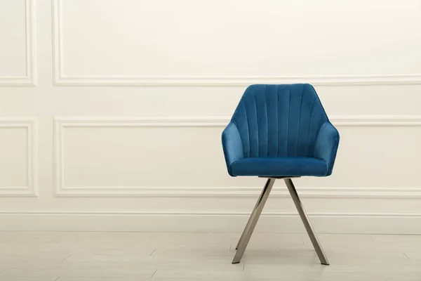 Modern blue armchair near white wall indoors. Space for text