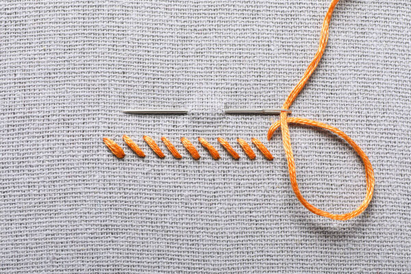 Needle with orange embroidery floss and row of stitches on grey fabric, top view