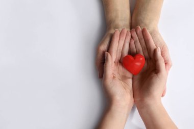 Beyaz arka planda kırmızı kalp taşıyan genç ve yaşlı kadınlar.