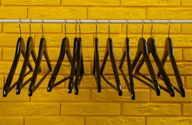 Sarı tuğla duvarın yanında birçok askısı olan gardırop rafı.