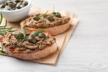 Lezzetli ezmeli ekmek dilimleri, kapari ve beyaz ahşap masada biberiye, yakın plan. Metin için boşluk