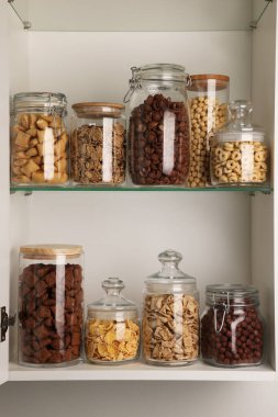 Raflarda farklı kahvaltı gevrekleri olan cam kaplar.
