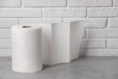 Roll of white paper towels on grey table near brick wall. Space for text
