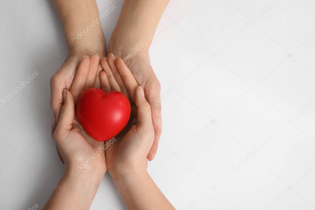 Young and elderly women holding red heart on white background, top view