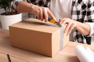 İçerideki ahşap masada paket açmak için bıçak kullanan adam, yakın plan.