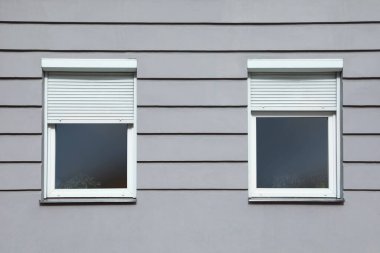 Wall of grey stone building with windows and rolling shutters
