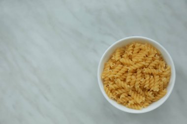 Beyaz mermer masa üzerinde pişmemiş fusilli makarna ile kase, üst manzara. Metin için boşluk