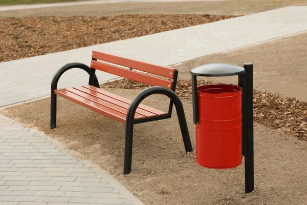 Şehir Parkında Ahşap Bankın Yanındaki Kırmızı Metal Çöp Tenekesi — Stok fotoğraf
