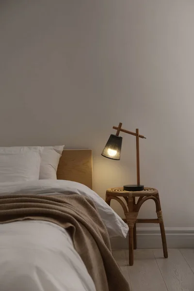 Stylish lamp on table near bed indoors