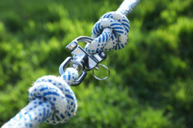 Climbing ropes with carabiner on blurred green background, closeup