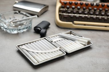 Tütün filtresi, sigara, çakmak ve cam kül tablası, gri masada antika daktilo, yakın plan.