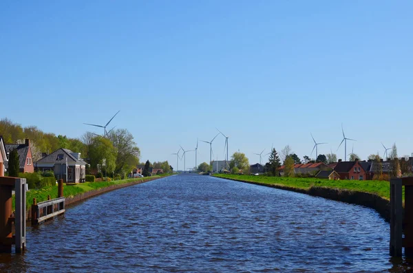 Beautiful small town with canal and wind turbines on sunny day. Alternative energy source