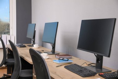Ofisin içini aç. Açık gri duvarın yanında bilgisayarları olan modern işyerleri