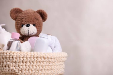 Bebek kozmetik ürünleri, banyo aksesuarları ve bej arka planda örgü sepetinde oyuncak ayı, yakın plan. Metin için boşluk