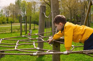 Küçük çocuk oyun bahçesinde ipe tırmanıyor.