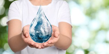 Dünya Su Günü. Bulanık yeşil arka planda Dünya görüntüsü olan bir damla simgesi tutan kadın, yakın plan.