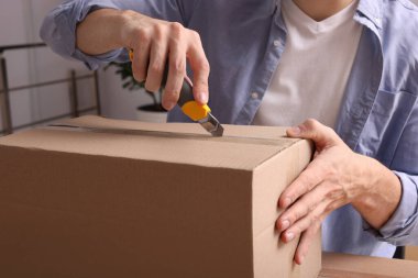 İçerideki ahşap masada paket açmak için bıçak kullanan adam, yakın plan.