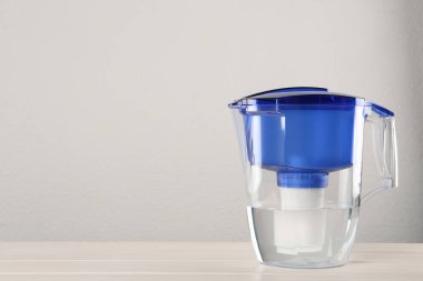Filter jug with purified water on white table against light background. Space for text