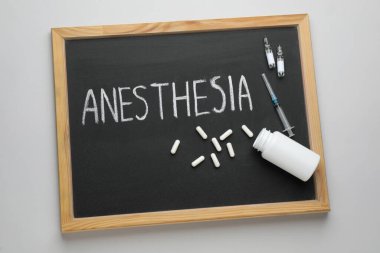 Blackboard with word Anesthesia, syringe and drugs on light grey background, top view
