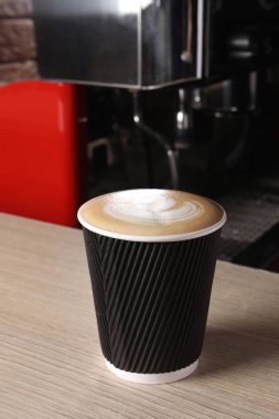 Takeaway paper cup of fresh aromatic coffee on wooden counter in cafe