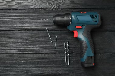 Modern electric power drill and different bits on black wooden table, flat lay. Space for text