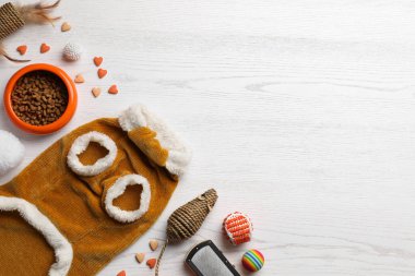 Beyaz ahşap masa üzerinde kedi kıyafetleri, yemek ve aksesuarlarla bezenmiş düz bir kompozisyon. Metin için boşluk