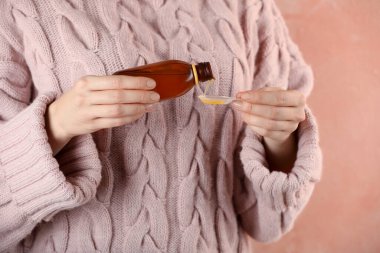 Öksürük şurubunu pembe arka planda kaşığa döken kadın, yakın plan.