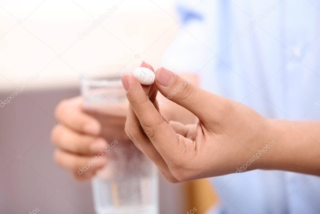 Calcium supplement. Woman holding pill and glass of water on blurred background, closeup