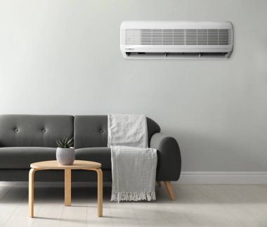 Beyaz duvarda modern klima ve şık gri kanepe.