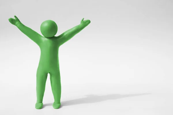 Human figure with arms wide open made of green plasticine on white background. Space for text