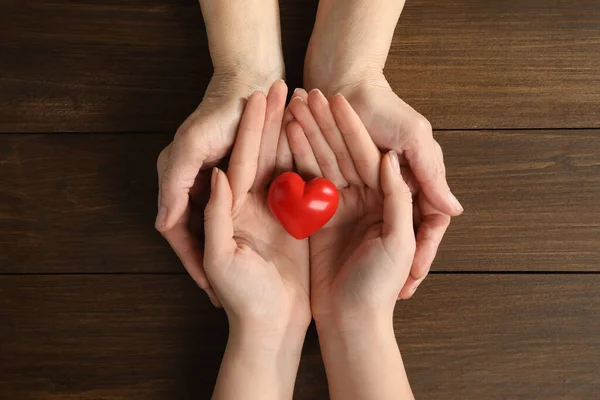 Genç ve yaşlı kadınlar kırmızı kalbi ahşap masada tutuyorlar.