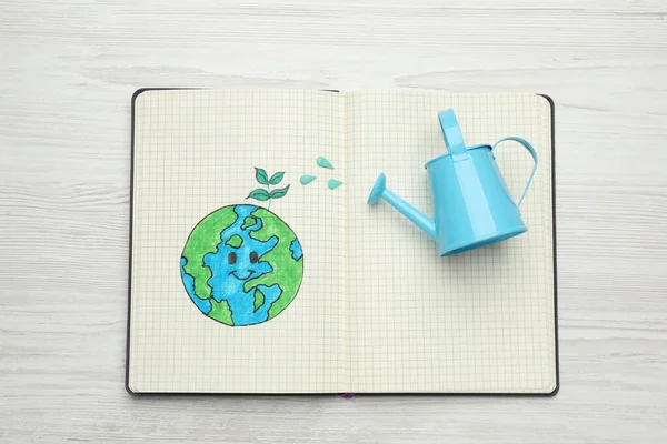 地球日快乐 带有行星图画和浇水的笔记本可以放在白色的木制桌子上 顶部看 — 图库照片