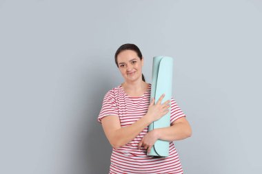 Gri arka planda yoga minderi olan mutlu şişman kadın.