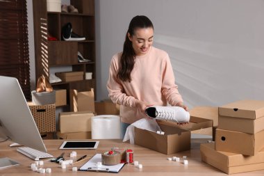 Seller packing shoes into cardboard box at table in office. Online store