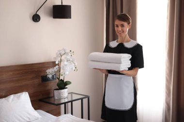 Otel odasında bir yığın temiz havlusu olan güzel oda hizmetçisi.