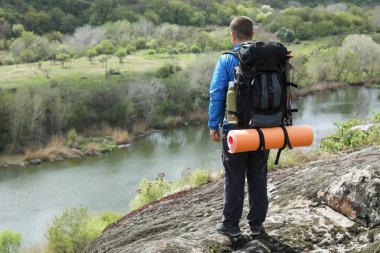 Sırt çantalı gezgin nehir kenarındaki kayalık tepede yolculuğa hazır.