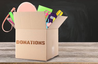 Tahtanın yanındaki ahşap masada farklı okul kırtasiyeleri olan bağış kutusu.