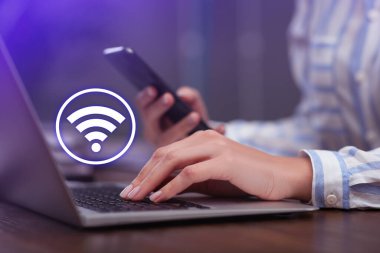 Akıllı telefon ve dizüstü bilgisayar kullanan bir kadın kapalı bir masadaki Wi-Fi 'ye bağlanıyor.